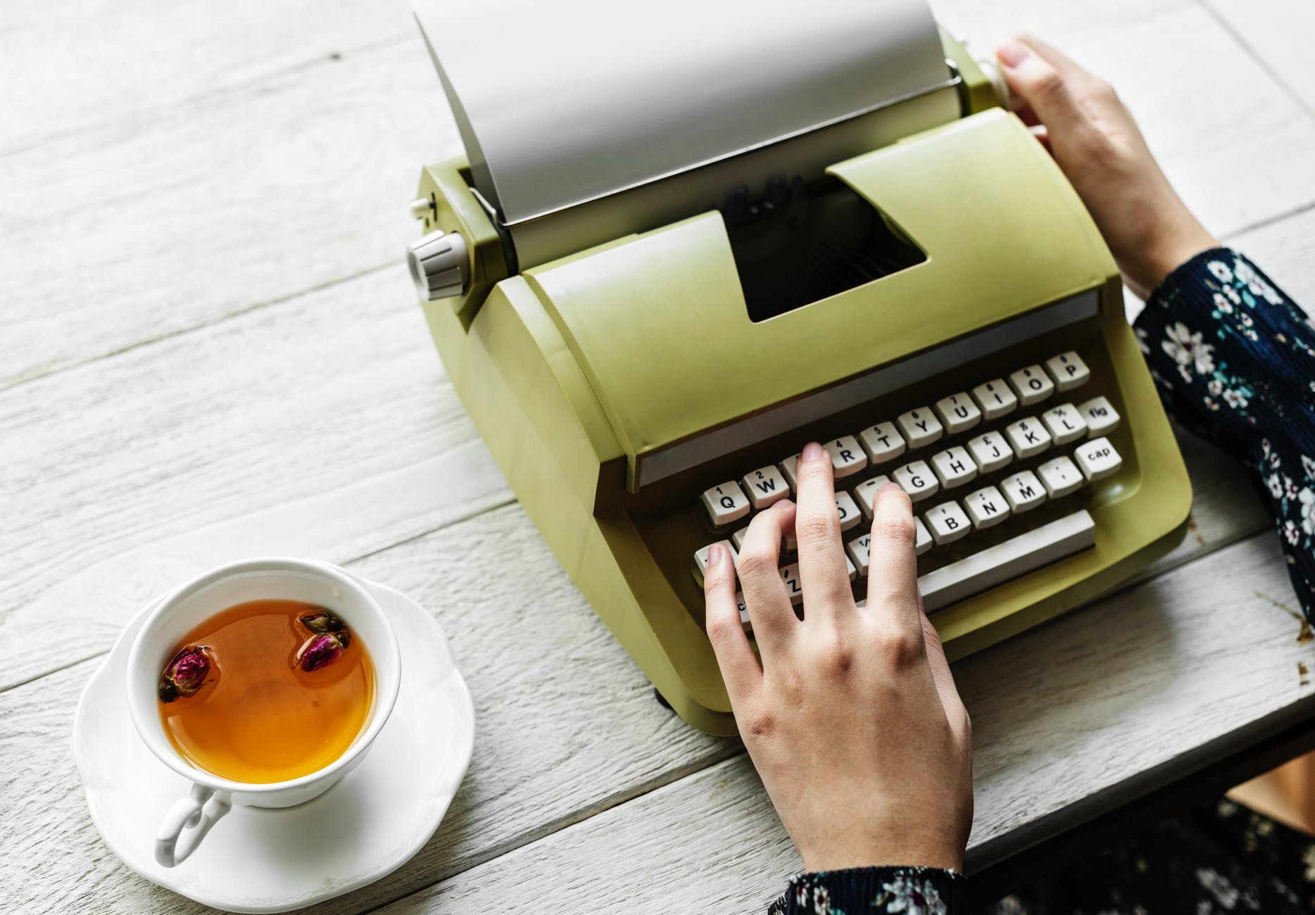 person holding type writer beside teacup and saucer on table