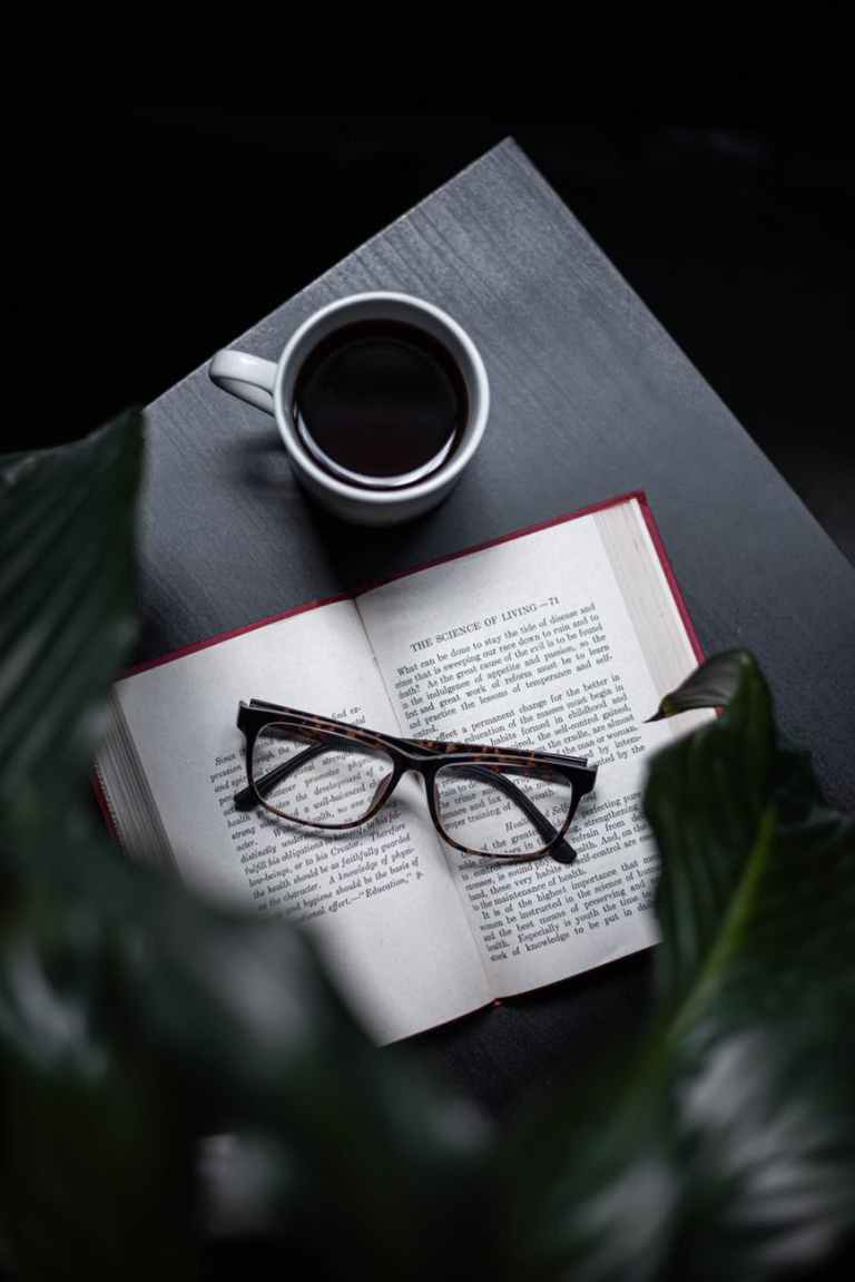 eyeglasses on opened book beside cup of coffee on table